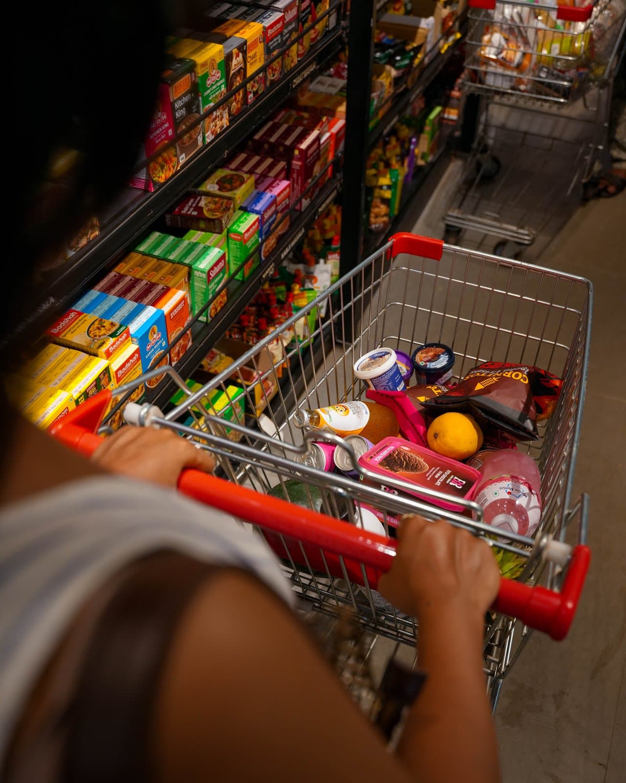 A shopper pushing a full trolley down a grocery aisle